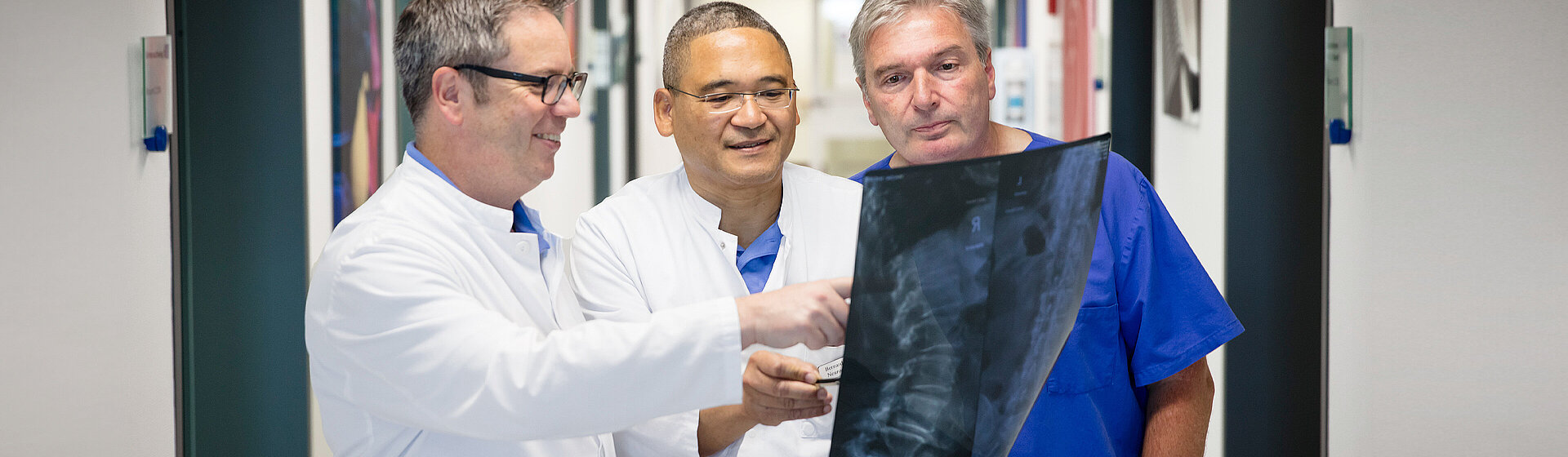 Drei Chirurgen schauen sich in der Neurochirurgie ein Röntgenbild der Wirbelsäule an