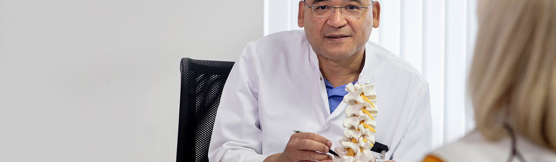 Arzt im Gespräch mit Patientin, hält ein Modell der Wirbelsäule – Symbol für neurochirurgische und orthopädische Beratung im MVZ